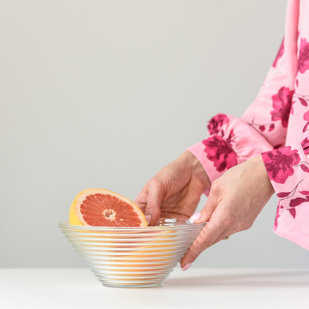 Kobieta przesuwająca miseczkę szklaną z grapefruitami po blacie w kuchni